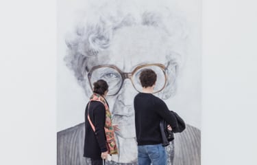 A couple walking by looking at a giant picture of an older woman on the wall